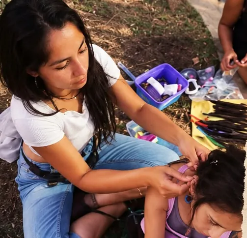 Nae tejiendo dreads a una niña al costado del camino